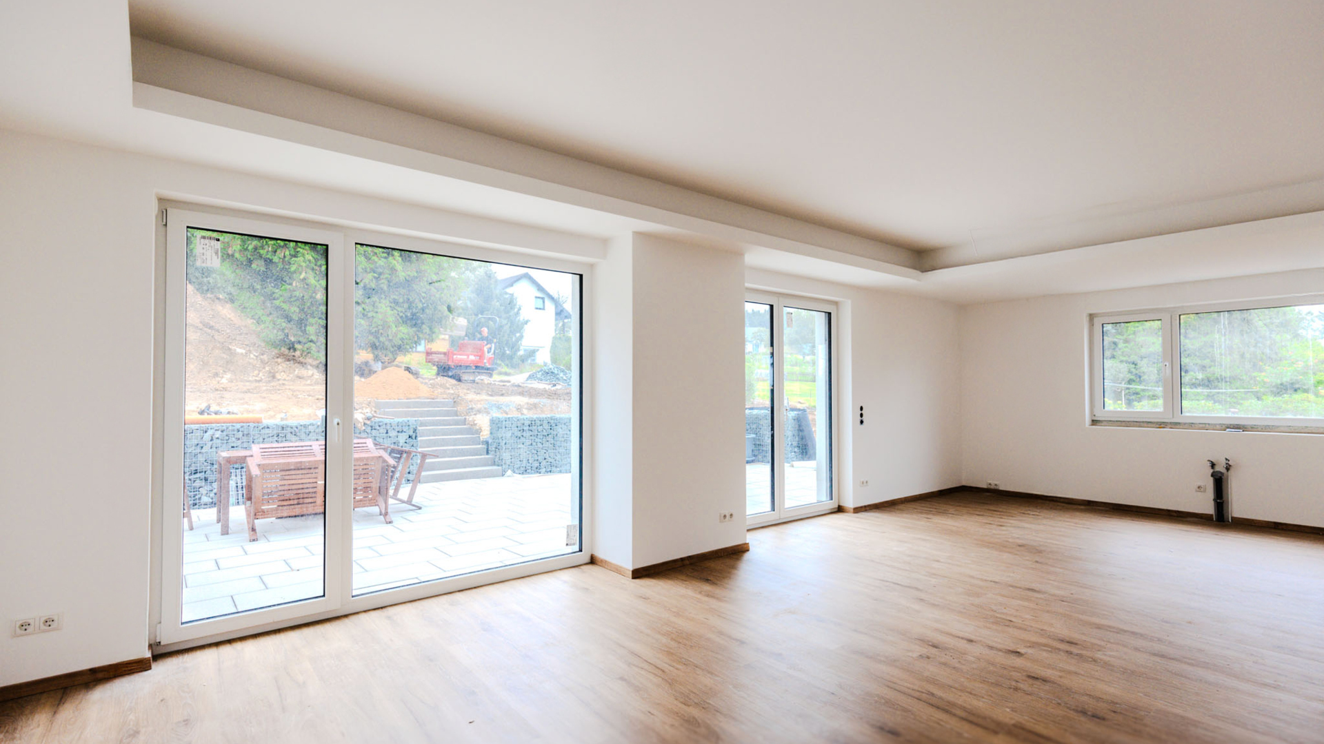 Großzügiges, lichtdurchflutetes Wohnzimmer im Neubau mit großen Glasschiebetüren zur Terrasse und indirekter Deckenbeleuchtung